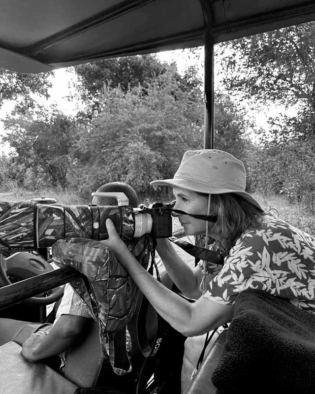 Schwarz-weiße Portrait Foto der Fotografin Barbara Westphalen, die seitlich durch ihre Kamera schaut. Sie sitzt in einem offenen Safariauto .