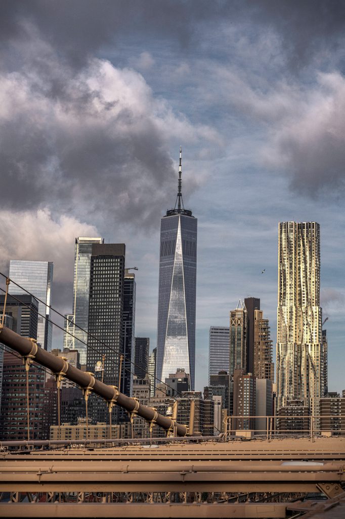 Skyline von Manhattan mit dem One World Trade Center, fotografiert von der Brooklyn Bridge vor stimmungsvollem Himmel.