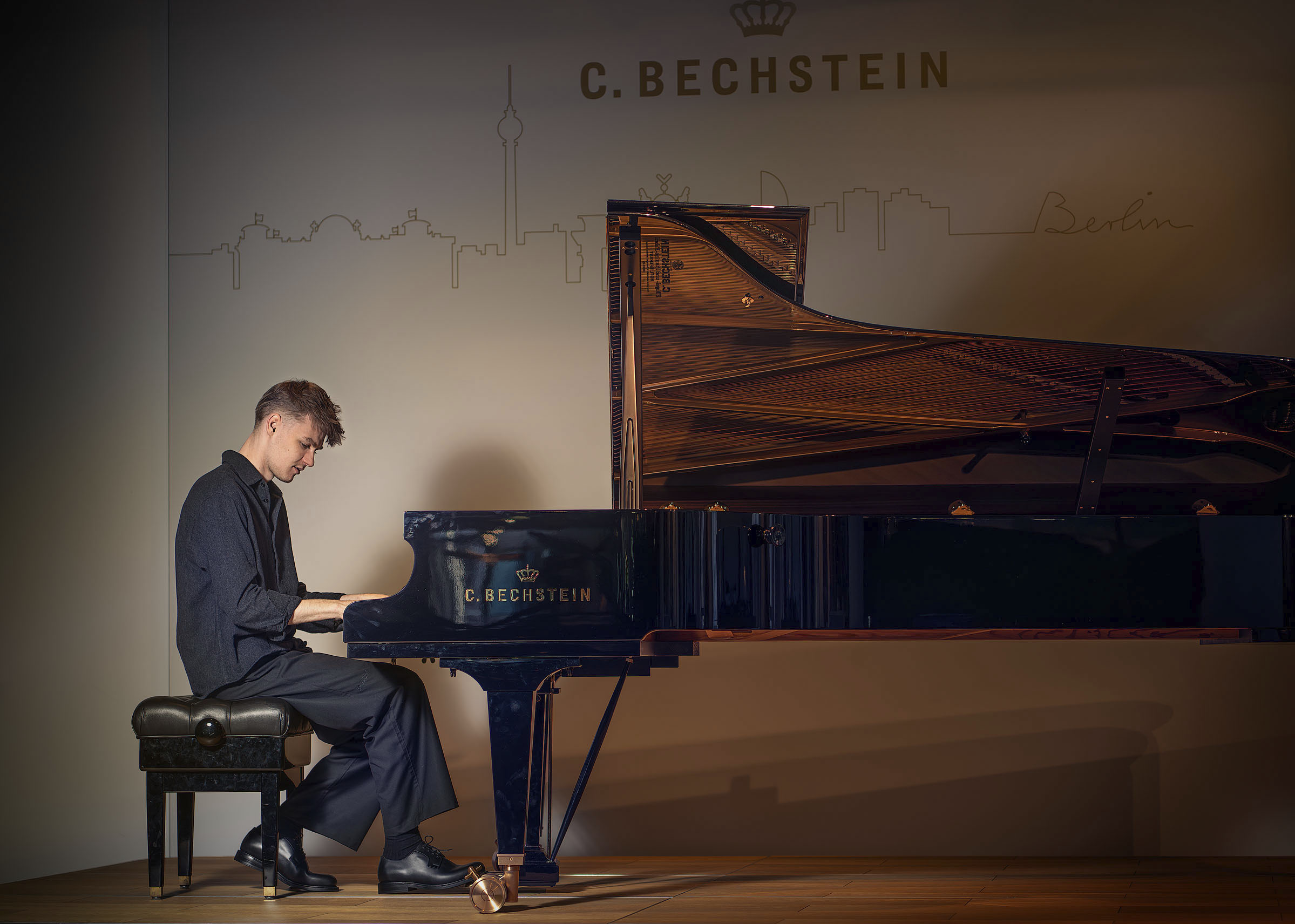 Atmosphärisches Künstlerporträt von Pianisten Janik Chêch in einer dunklen Kulisse. Er spielt am Flügel positioniert, der durch gezielte Beleuchtung hell erstrahlt und im starken Kontrast zur tiefen, schattigen Umgebung steht. Die geheimnisvolle und fokussierte Lichtstimmung betont die Verbindung zwischen Musiker und Instrument.