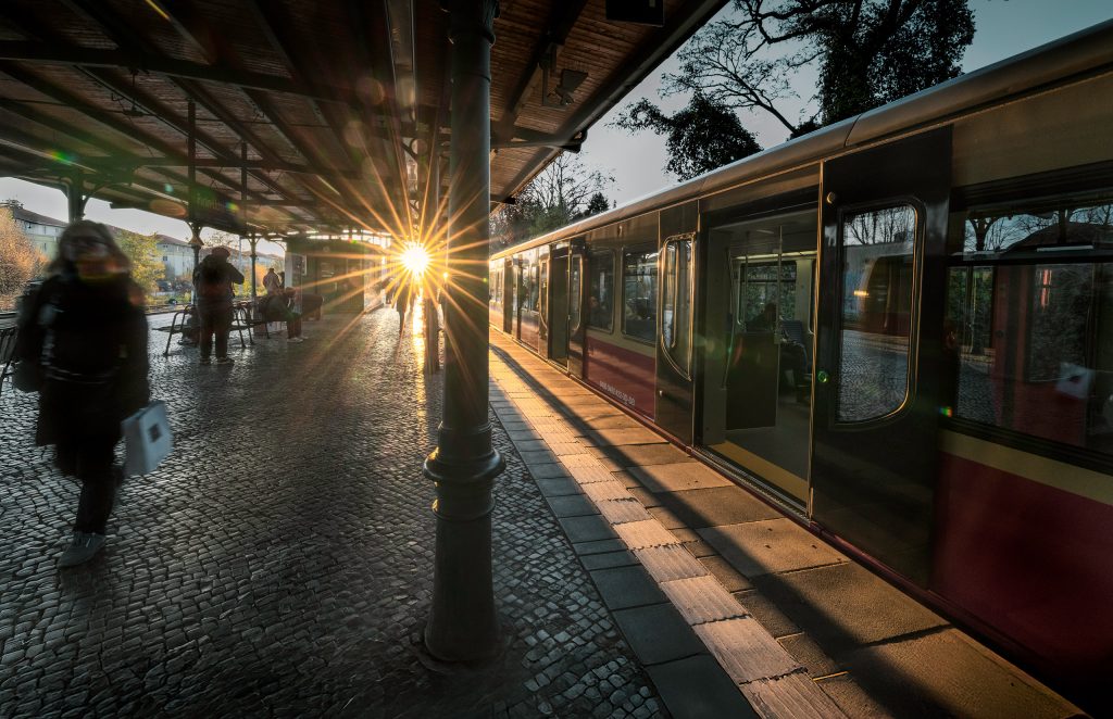 Berliner S-Bahn-Station Lichterfelde West im Herbst: Fahrgäste verlassen den Bahnsteig neben einer eingefahrenen S-Bahn. Die tiefstehende Sonne erzeugt einen markanten Sonnenstern unter dem Bahnhofsdach.