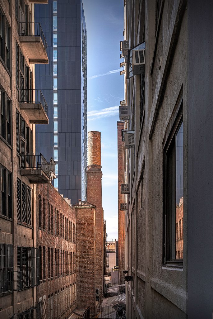 Fine-Art-Architekturfotografie aus New York: Blick durch die tiefen Gebäudeschluchten von Wolkenkratzern, die in der Mitte nur einen schmalen Streifen des Himmels freigeben.
