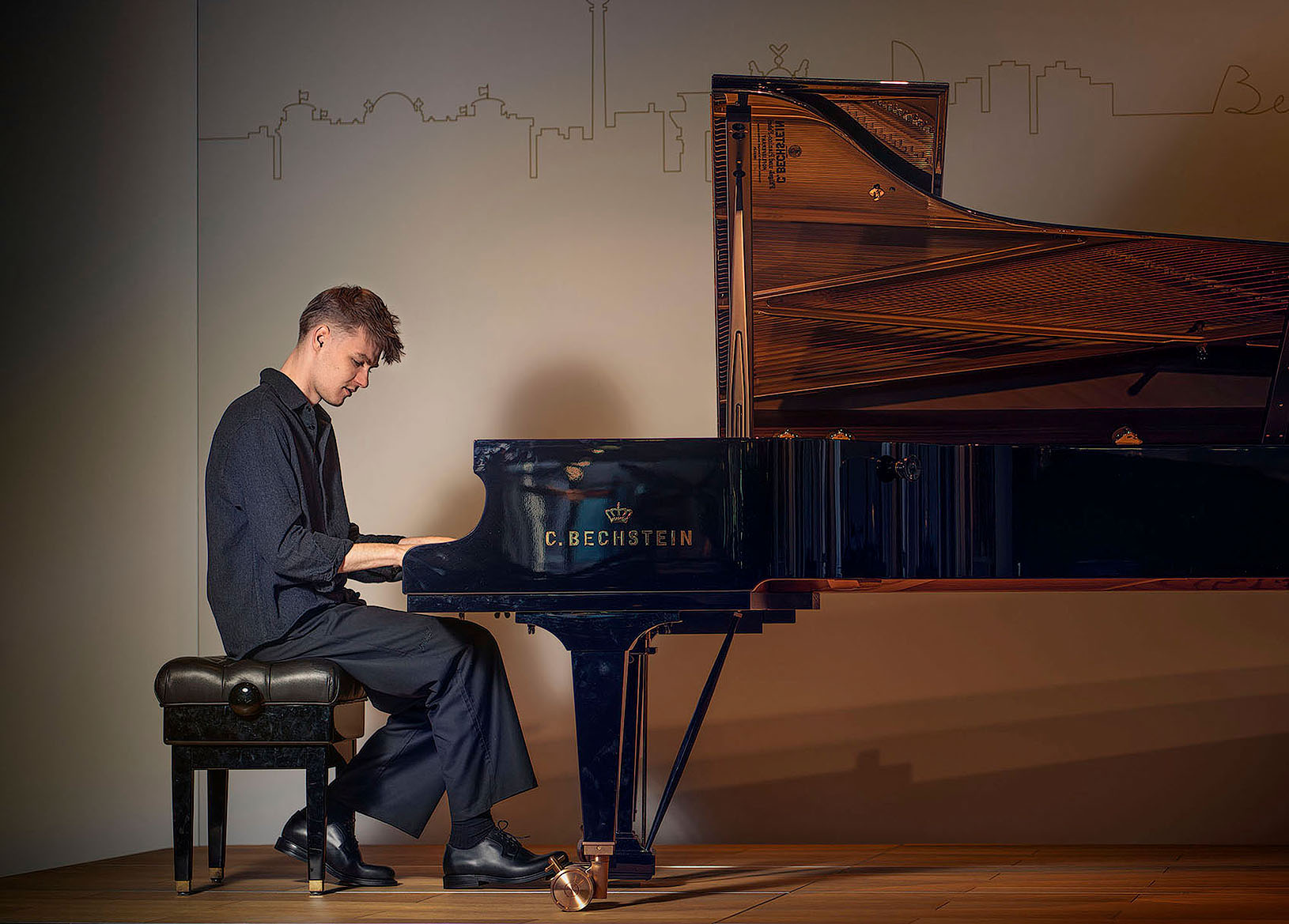 Atmosphärisches Künstlerporträt von Pianisten Janik Chêch in einer dunklen Kulisse. Er spielt am Flügel positioniert, der durch gezielte Beleuchtung hell erstrahlt und im starken Kontrast zur tiefen, schattigen Umgebung steht. Die geheimnisvolle und fokussierte Lichtstimmung betont die Verbindung zwischen Musiker und Instrument.