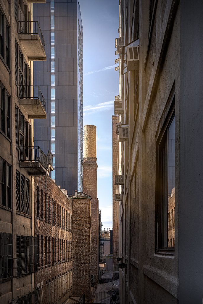 Fine-Art-Architekturfotografie aus New York: Blick durch die tiefen Gebäudeschluchten von Wolkenkratzern, die in der Mitte nur einen schmalen Streifen des Himmels freigeben.